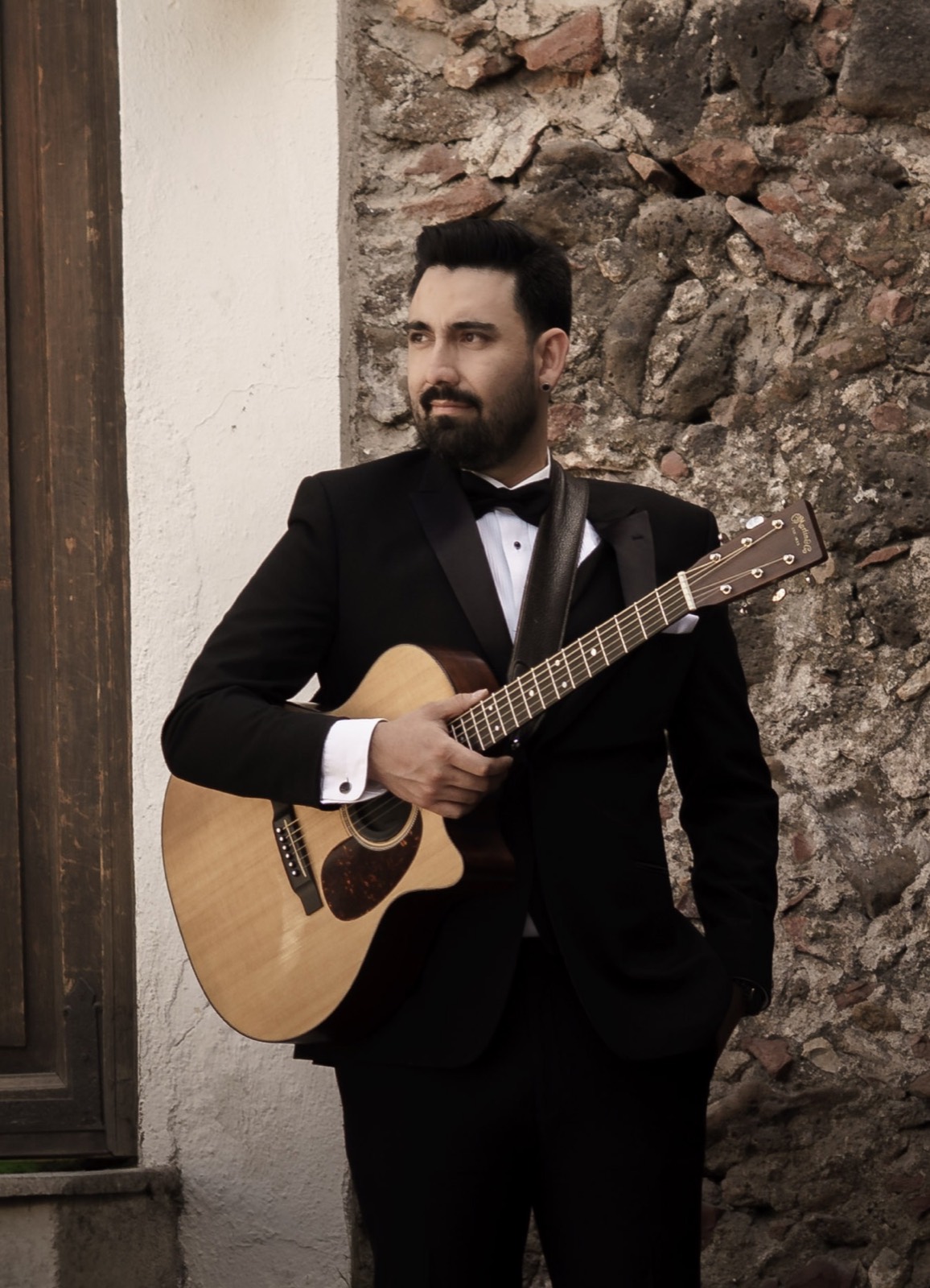 Adrián Eugenio interpreta guitarra con vestimenta formal.